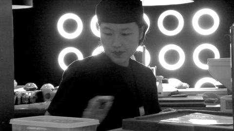 Black-and-white photograph of a person behind a counter, with illuminated circles in the background